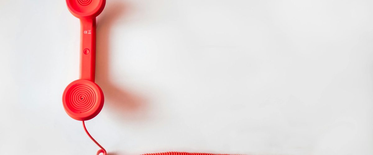 Vintage red phone handset with coiled cable on a clean white background, classic communication device.